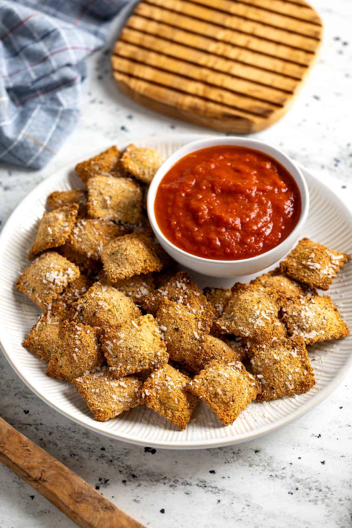 Toasted ravioli sprinkled with Parmesan on a plate with marinara sauce.