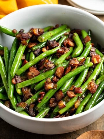 A serving bowl of green beans, bacon, and onions.