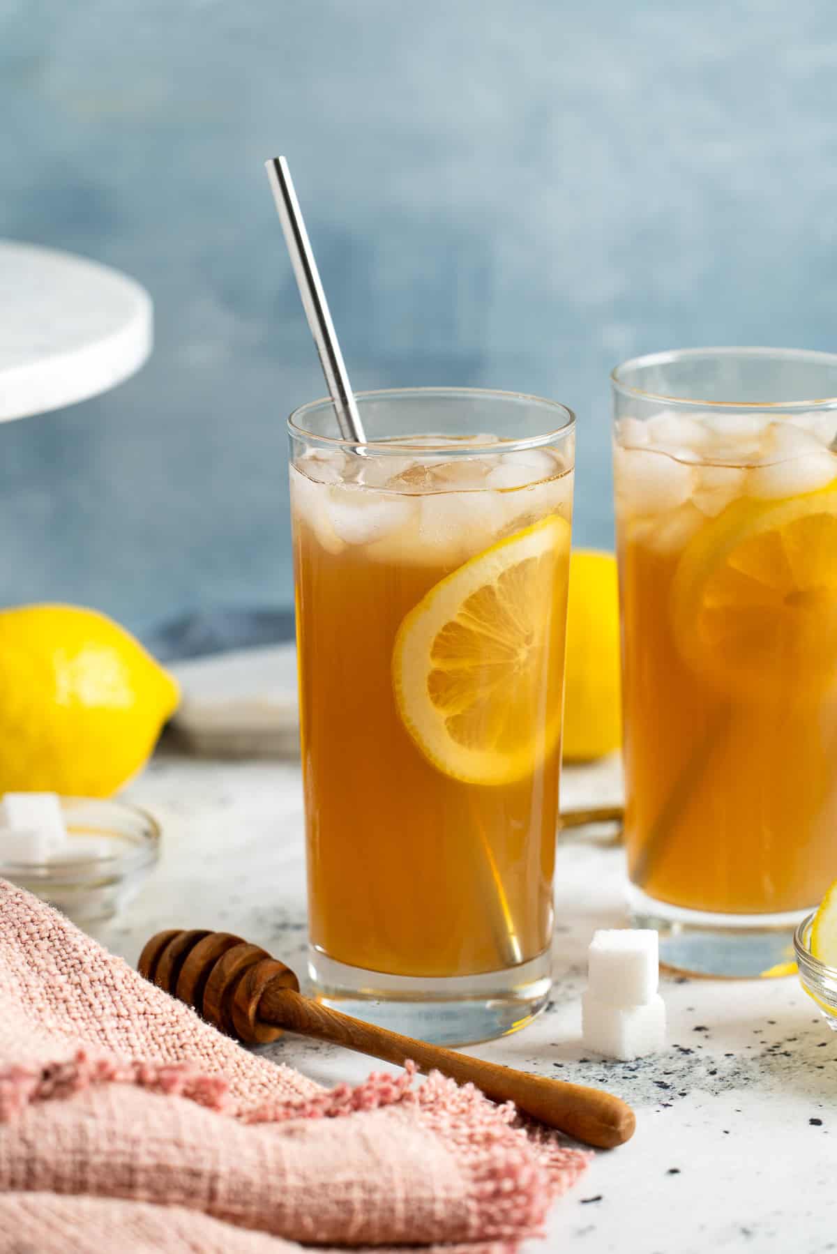 Two limoncello iced teas with straws and lemon rounds in highball glasses.