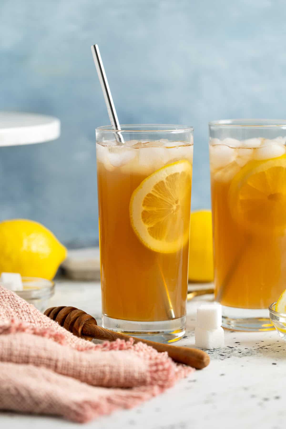 Two limoncello iced teas with straws and lemon rounds in highball glasses.