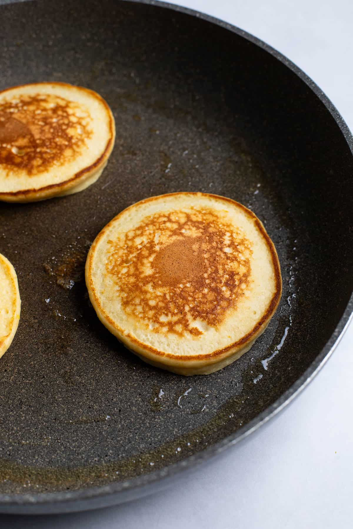 A batch of ricotta pancakes cooking in a pan.
