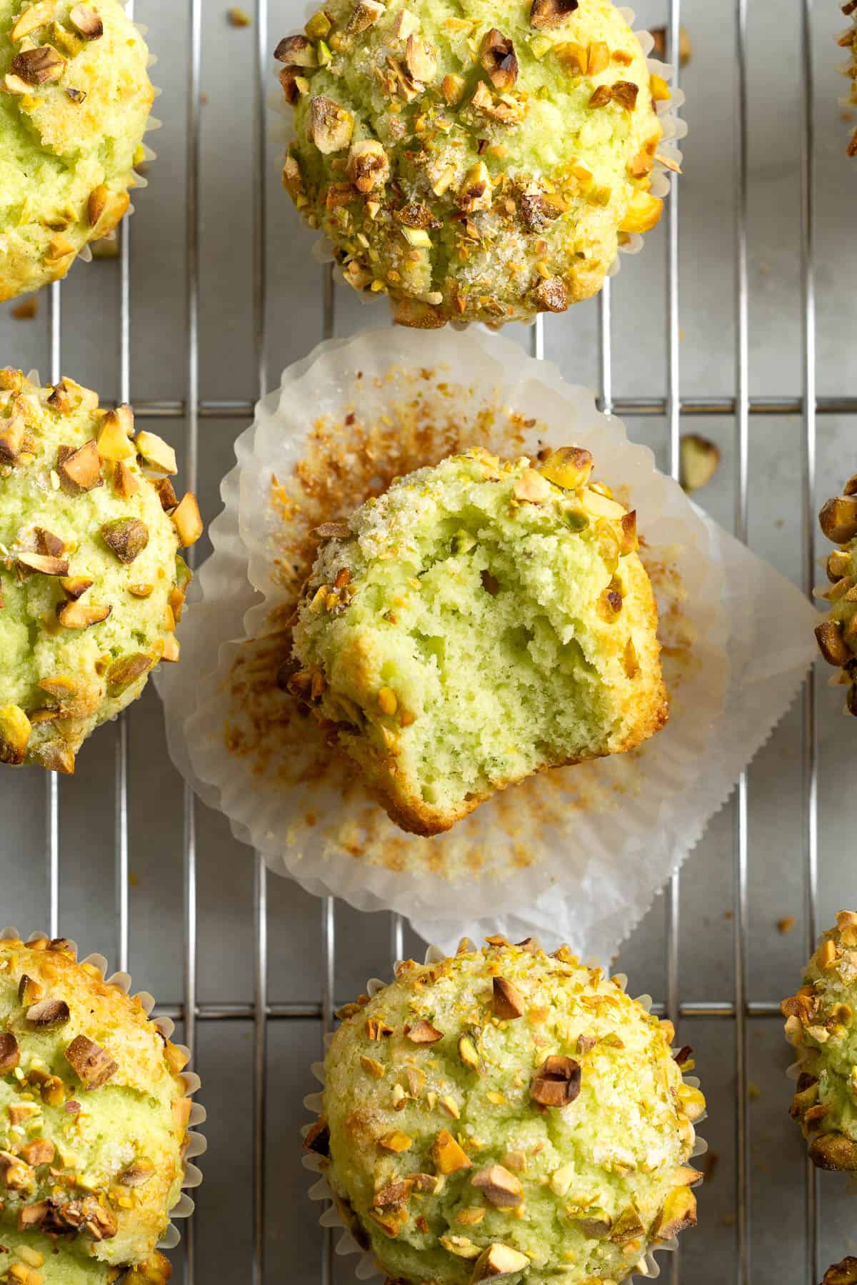Pistachio muffins on a cooling rack with a bite taken out of the center muffin.