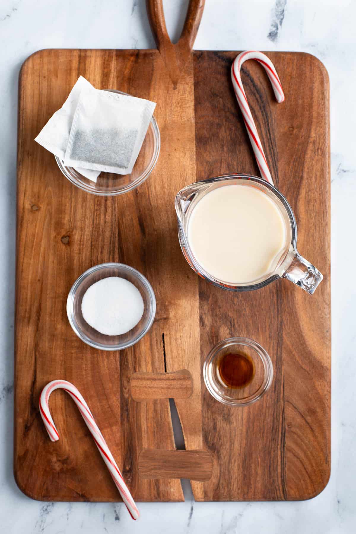 Peppermint tea latte ingredients in separate containers: tea bags, milk, vanilla extract, and sugar.