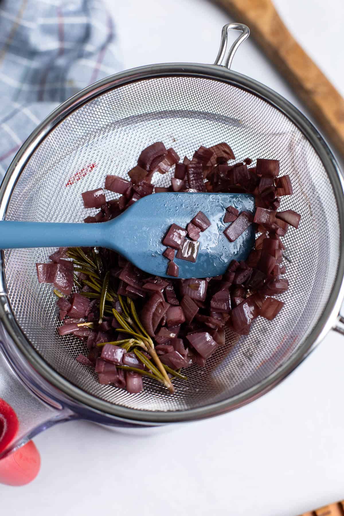 The jus poured through a metal sieve and a spatula pressing the shallots to release all jus.
