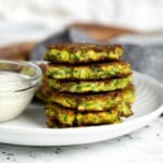 A stack of pan fried Italian-style zucchini fritters on a plate next to a bowl of dipping sauce.