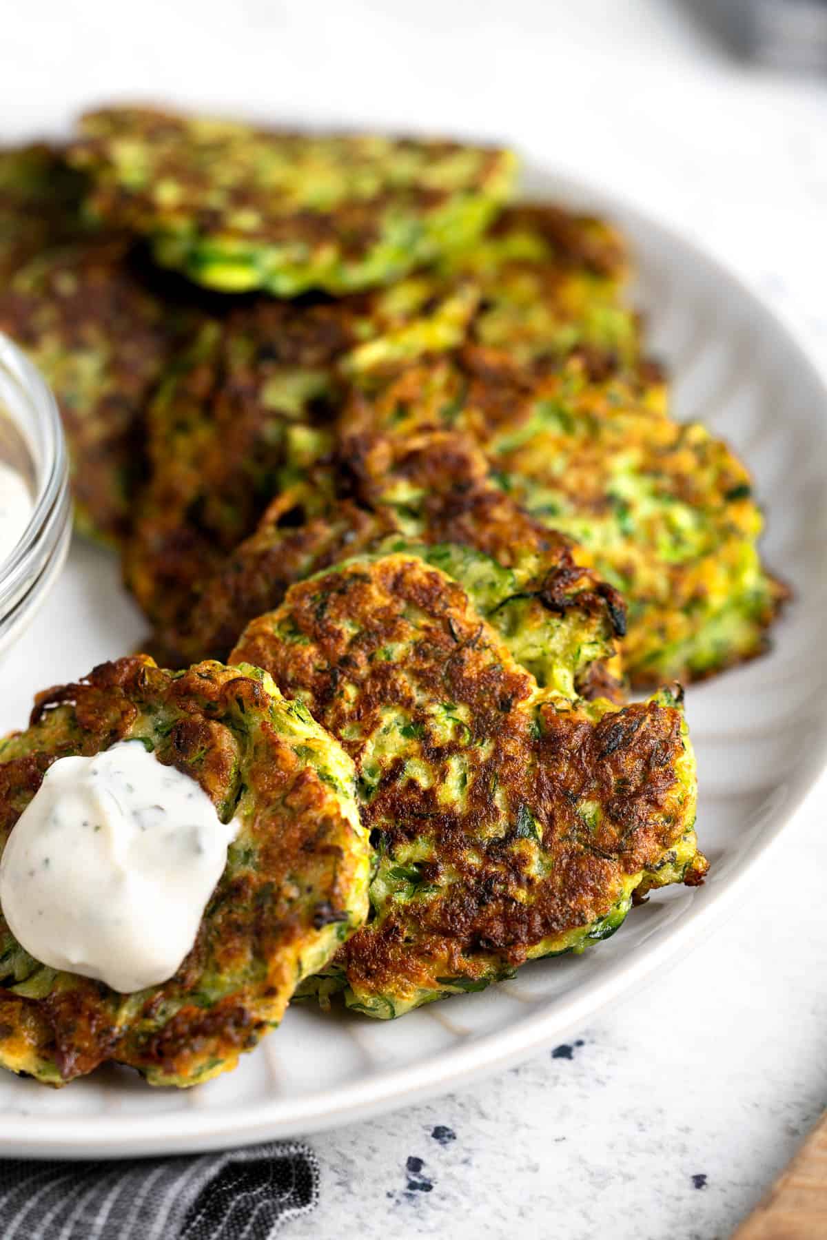 Zucchini fritters on a plate with a sour cream dipping sauce.