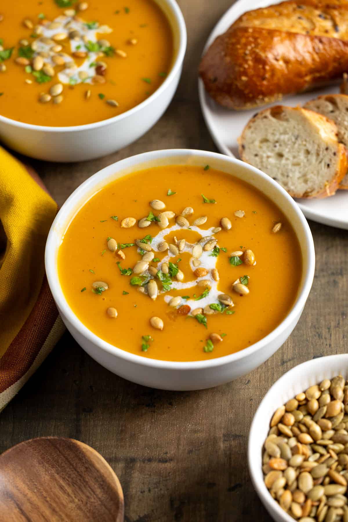 A bowl of pureed sweet potato soup topped with a coconut milk swirl, sunflower seeds, and herbs.