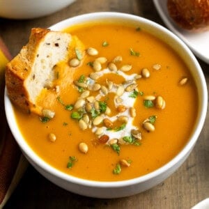 A bowl of sweet potato soup with a fresh baguette slice dipped into it.