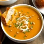 A bowl of pureed sweet potato soup topped with a coconut milk swirl, sunflower seeds, and herbs.