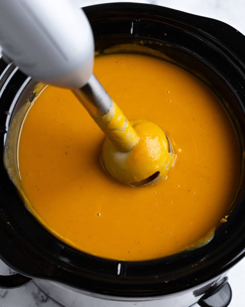 An immersion blender in the slow cooker of pureed, smooth soup.