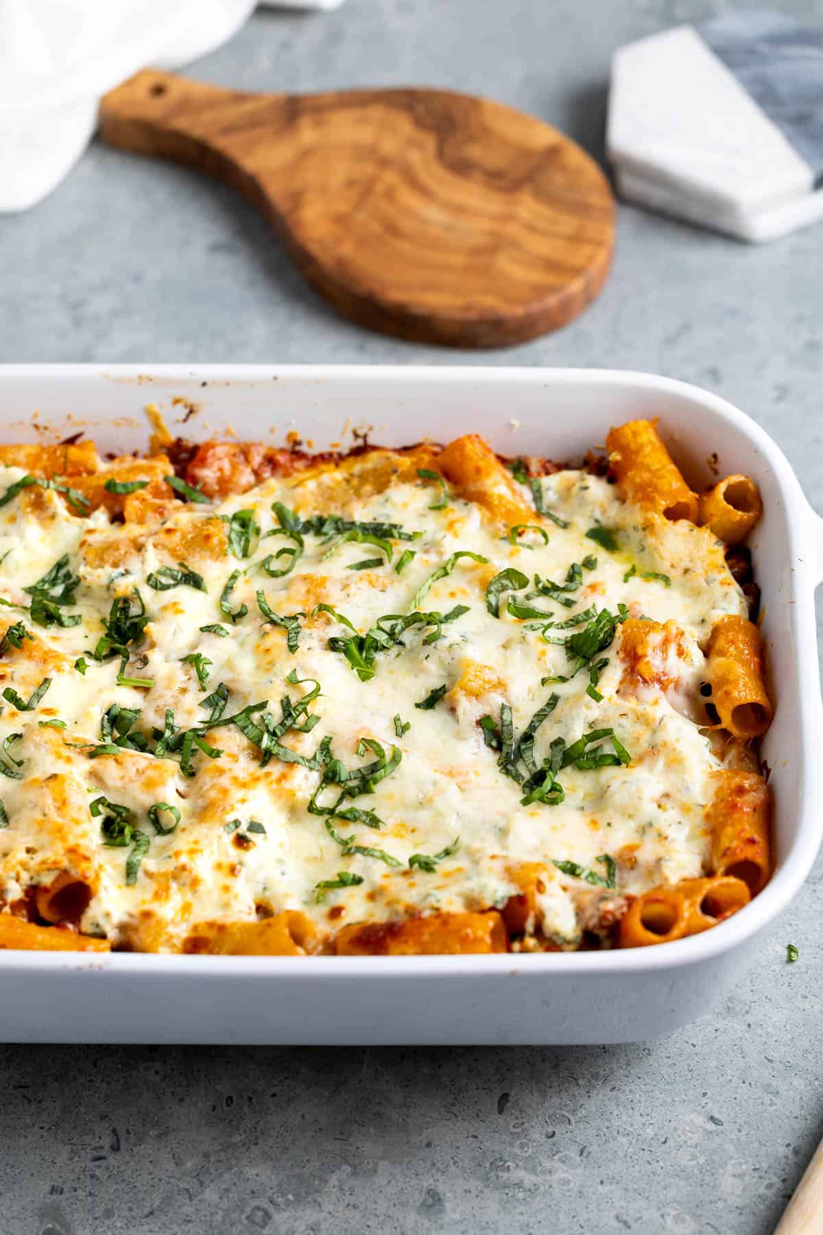 A baking dish filled with pasta al forno topped with melted cheese and fresh basil.