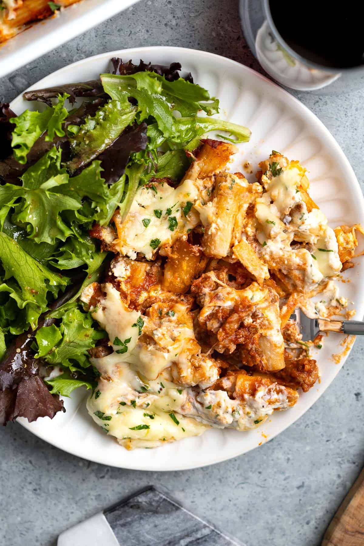 A serving of pasta al forno on a plate with a mixed greens salad.