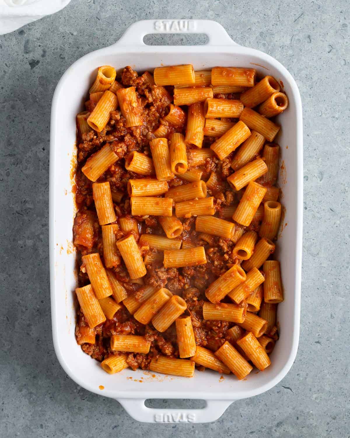 Meat sauce and cooked rigatoni added to a large rectangular baking dish.