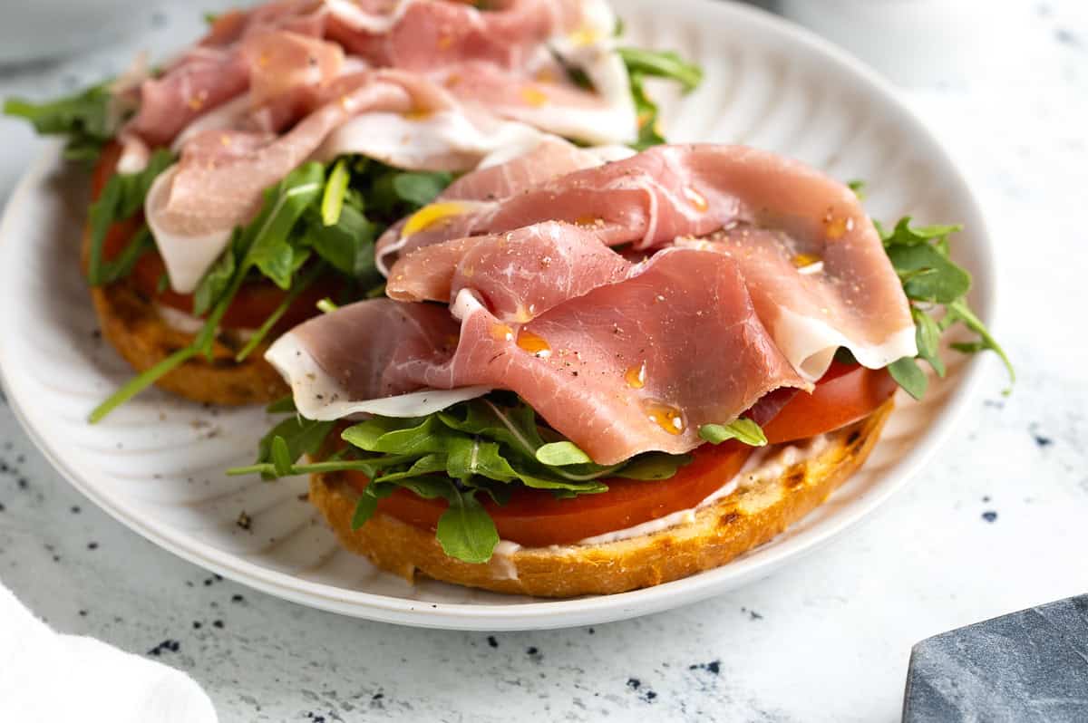 An open-face prosciutto sandwich on a plate.