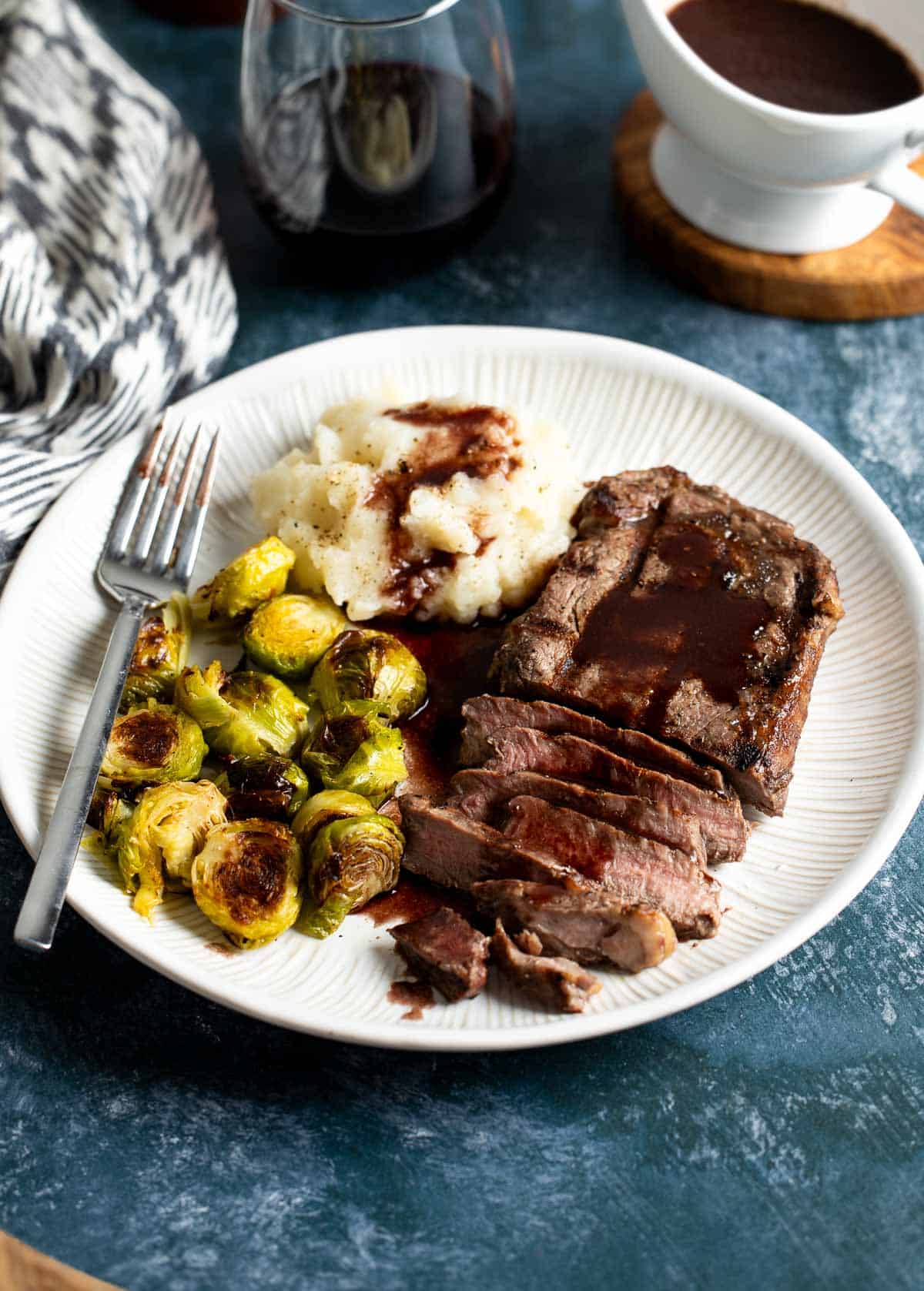 A plate of mashed potatoes, brussels sprouts, and steak served with red wine jus.