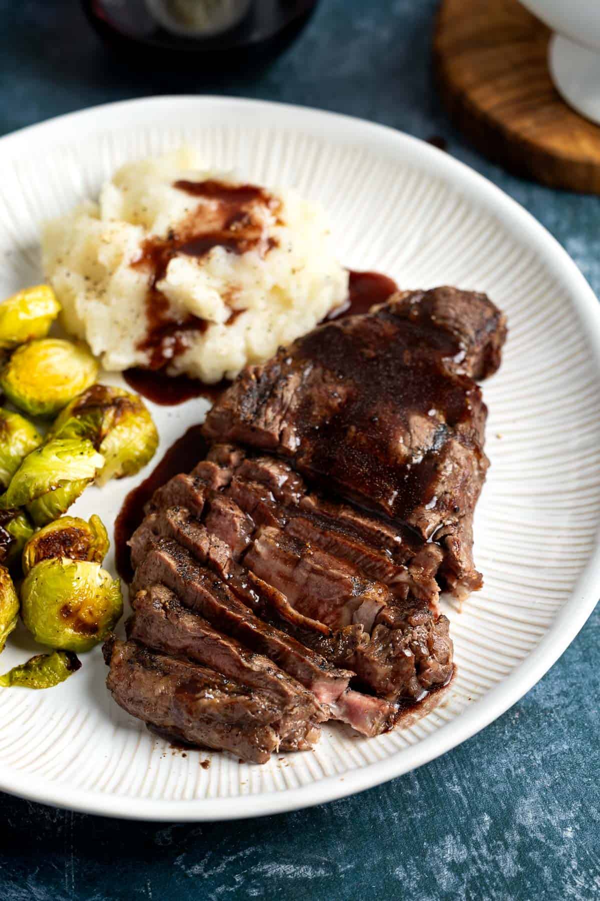 A plate of mashed potatoes, brussels sprouts, and steak served with red wine jus.