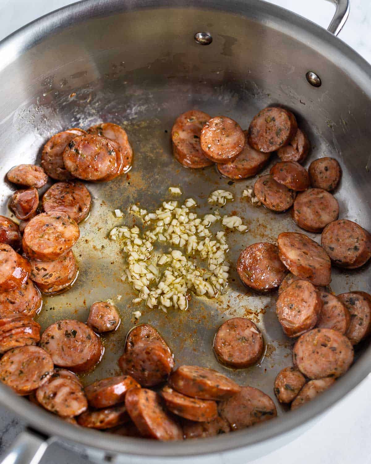 Chopped garlic cooking in the middle of the pan around the sausage.