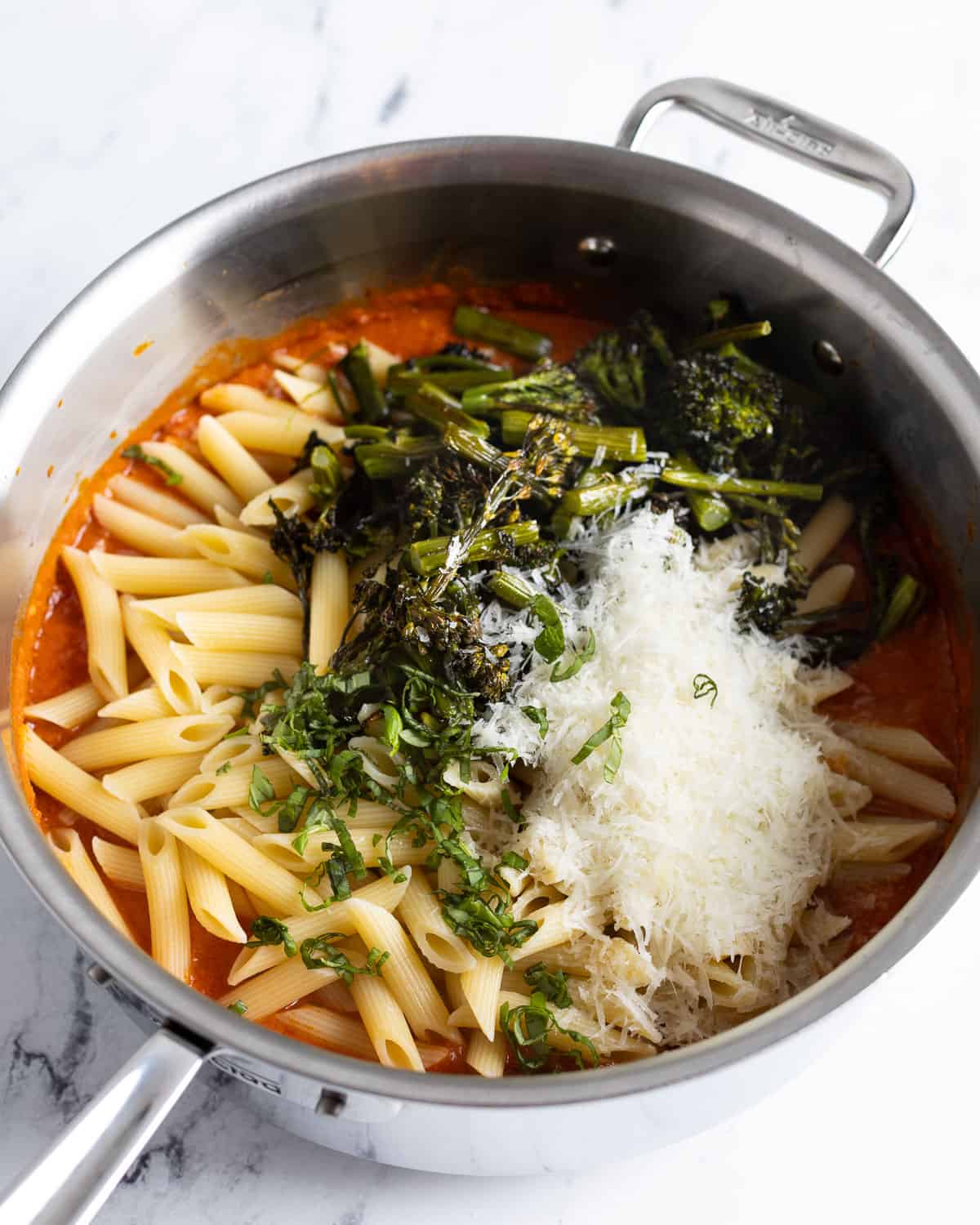 Cooked pasta, broccolini, basil, and cheese added to the pan.