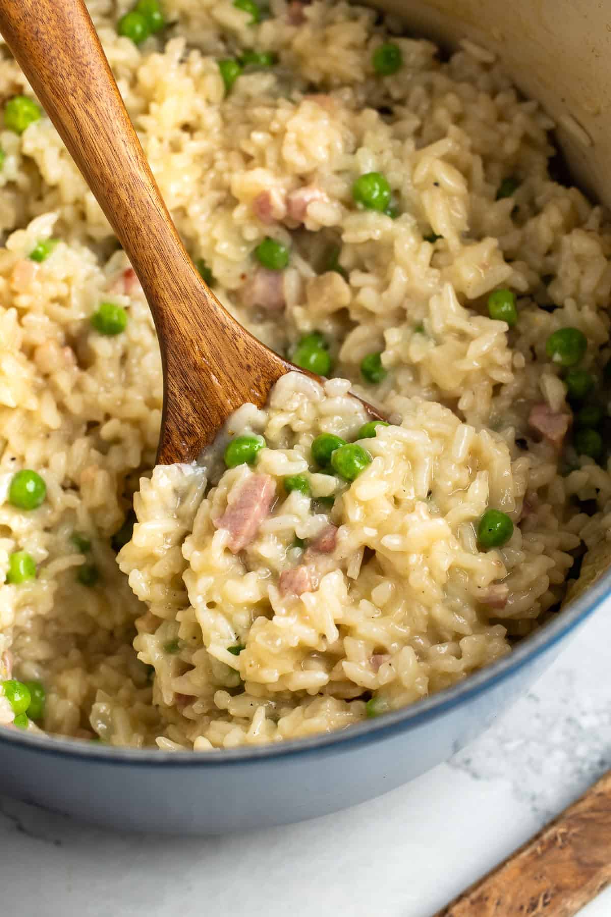 A wooden serving spoon scooping risotto from the Dutch oven.