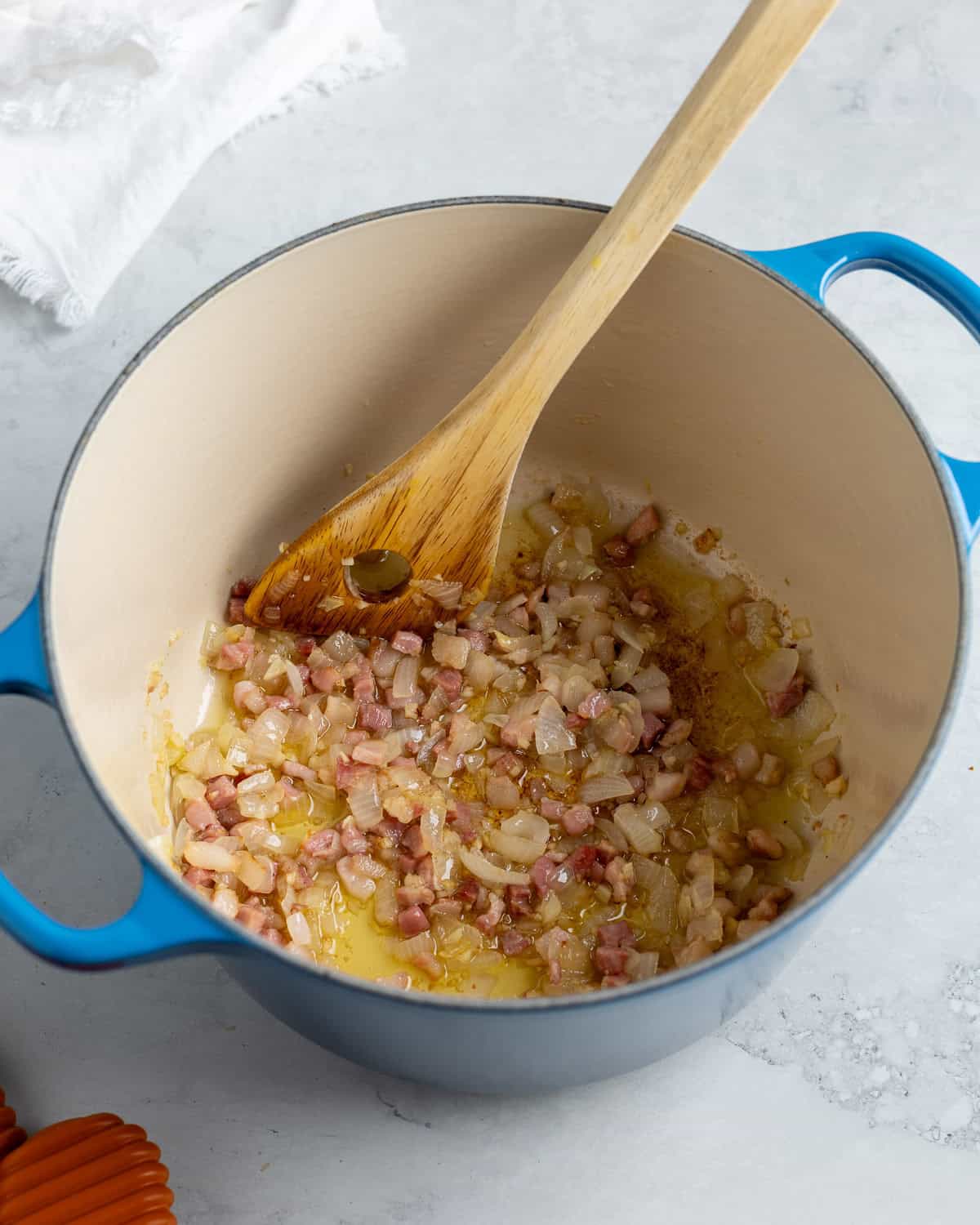 Diced onion, pancetta, and garlic cooking in oil in a Dutch oven.