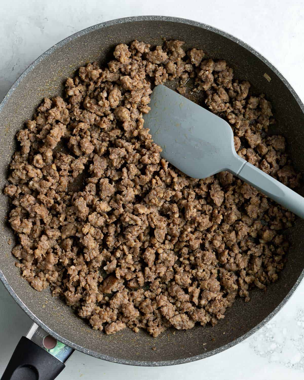Cooked and crumbled sausage in a skillet with a spatula.
