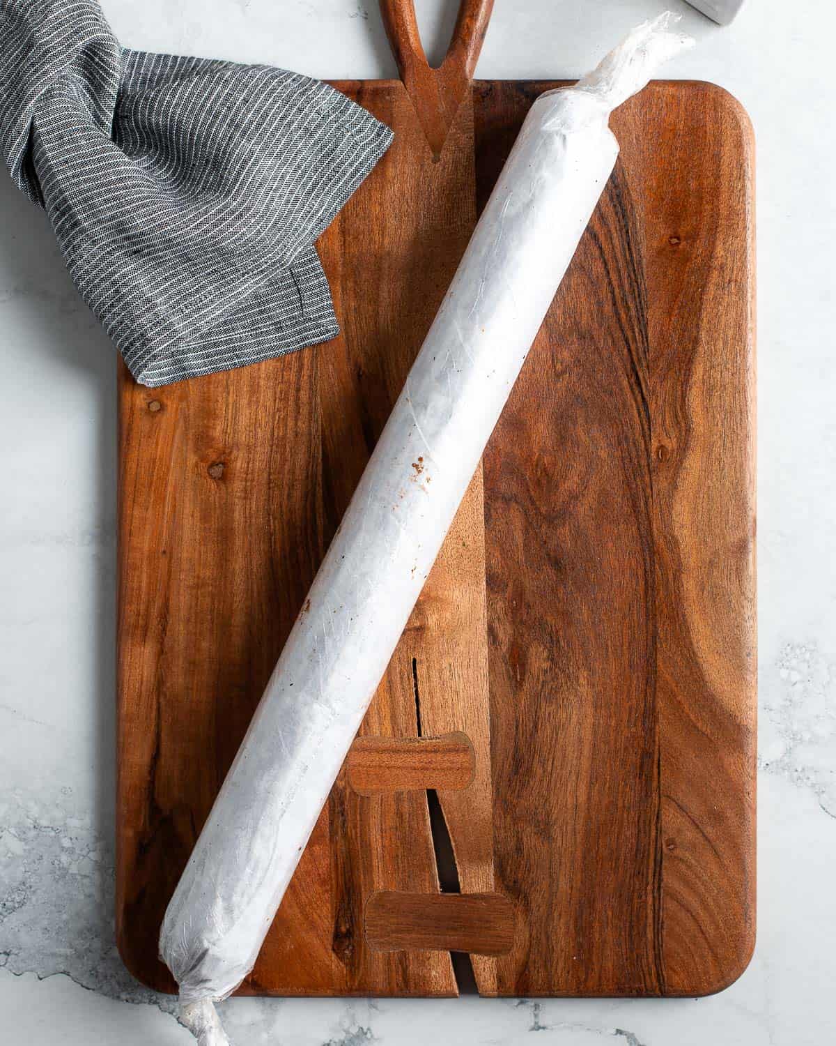 A round and hardened chocolate salami covered in parchment paper and plastic wrap.