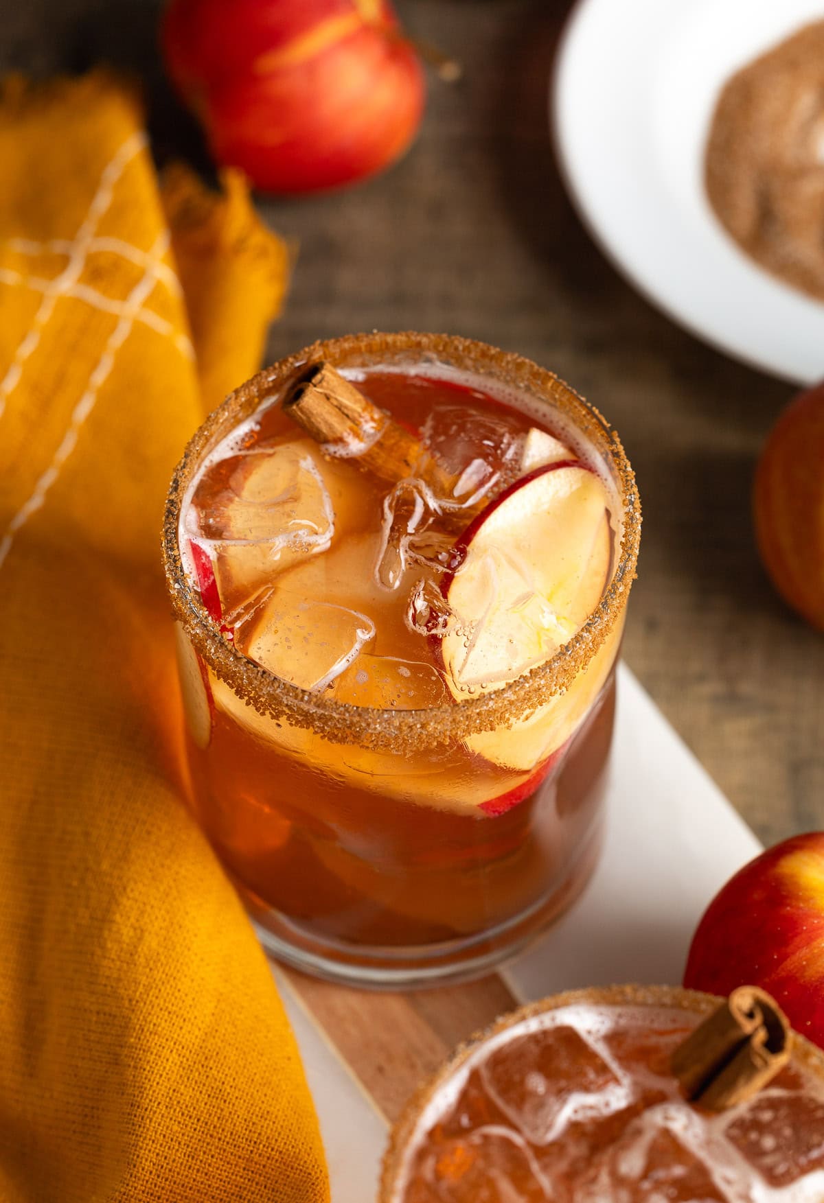 A sparkling apple cider mocktail in a rocks glass with ice, cinnamon sticks, and apple slice garnishes.