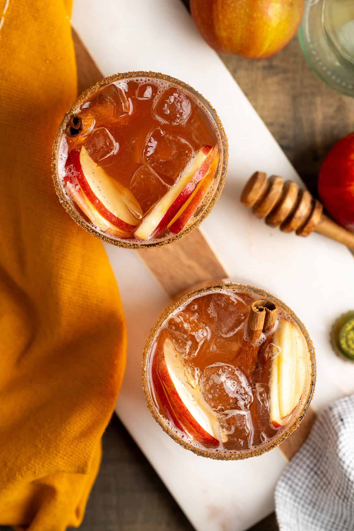 Two apple cider mocktails in cinnamon sugar rimmed glasses.