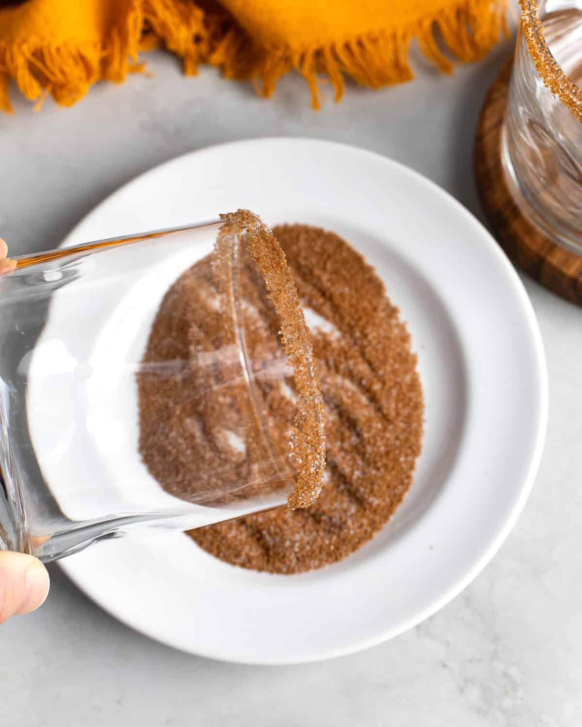 The rim of a rocks glass being pressed into a cinnamon sugar mixture.