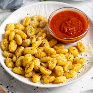 Parmesan-sprinkled air fryer gnocchi on a plate with a bowl of marinara sauce.
