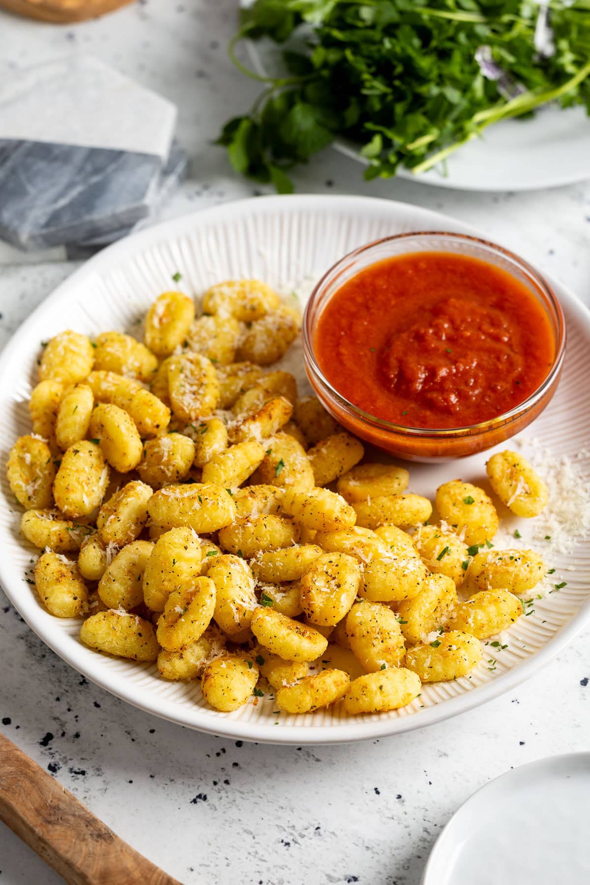 Parmesan-sprinkled air fryer gnocchi on a plate with a bowl of marinara sauce.