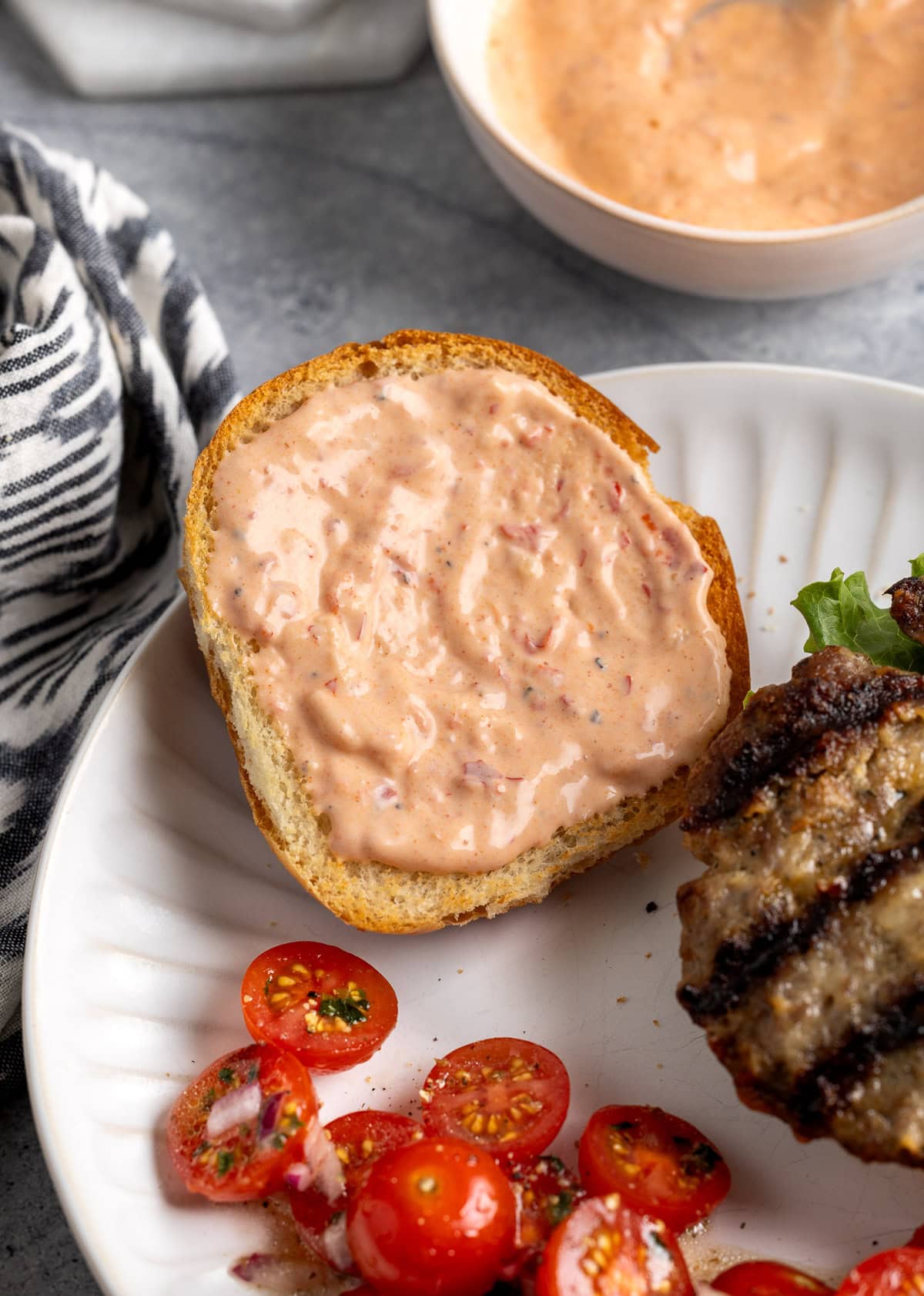 Calabrian aioli slathered on the top half of a sliced hamburger bun.