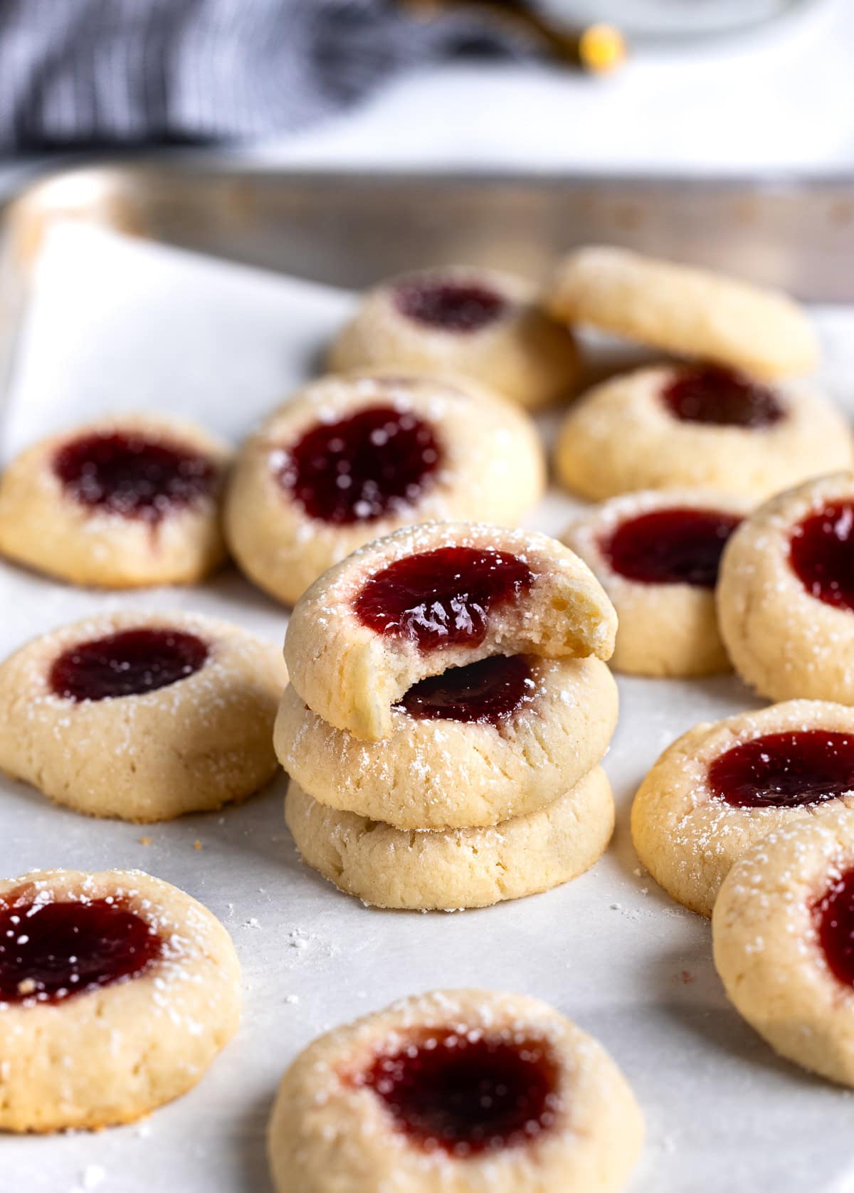 Thumbprint cookies stacked on a sheet pan after dusting with confectioners' sugar.