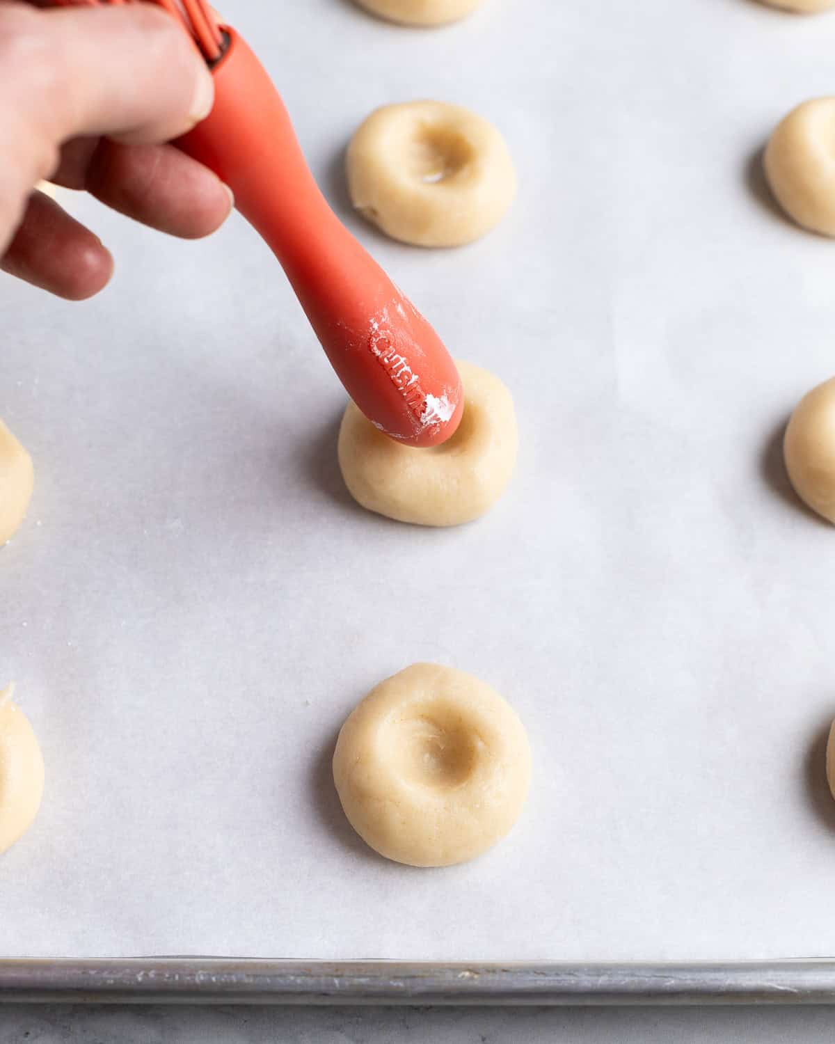 The rounded end of a whisk being pressed into cookie dough balls on a sheet pan.