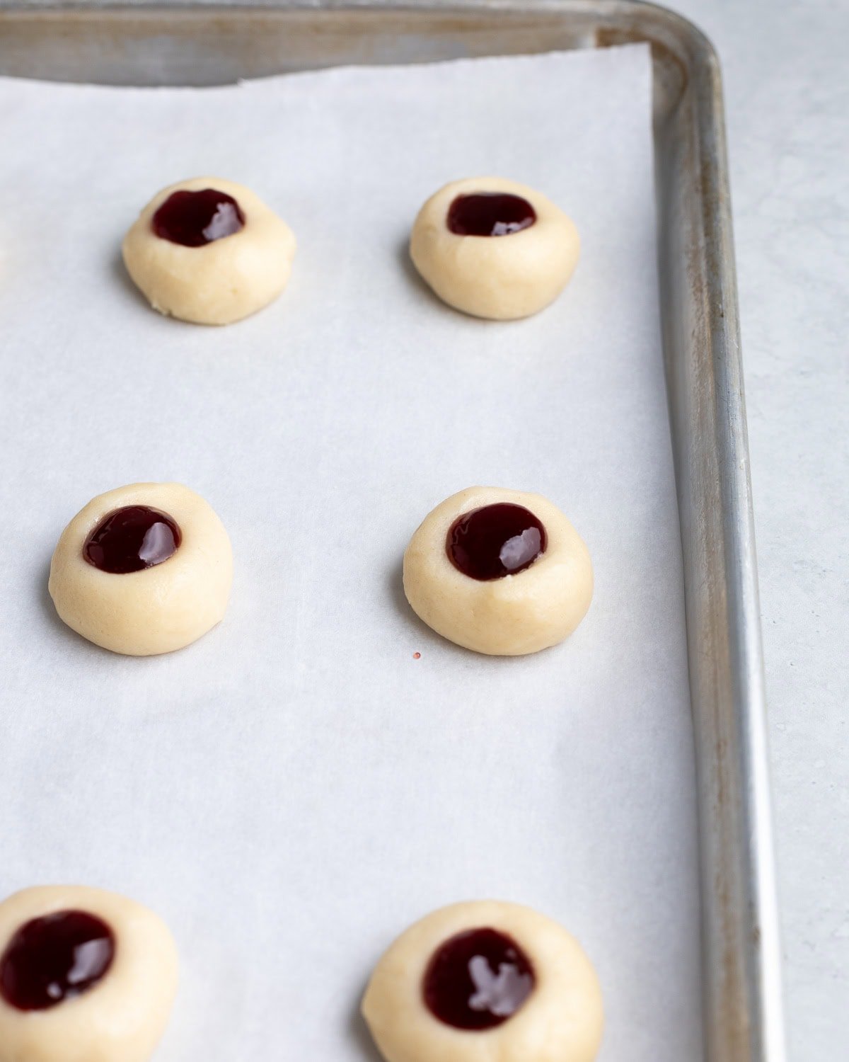 Thumbprint cookies filled with raspberry jam on a sheet pan before baking.