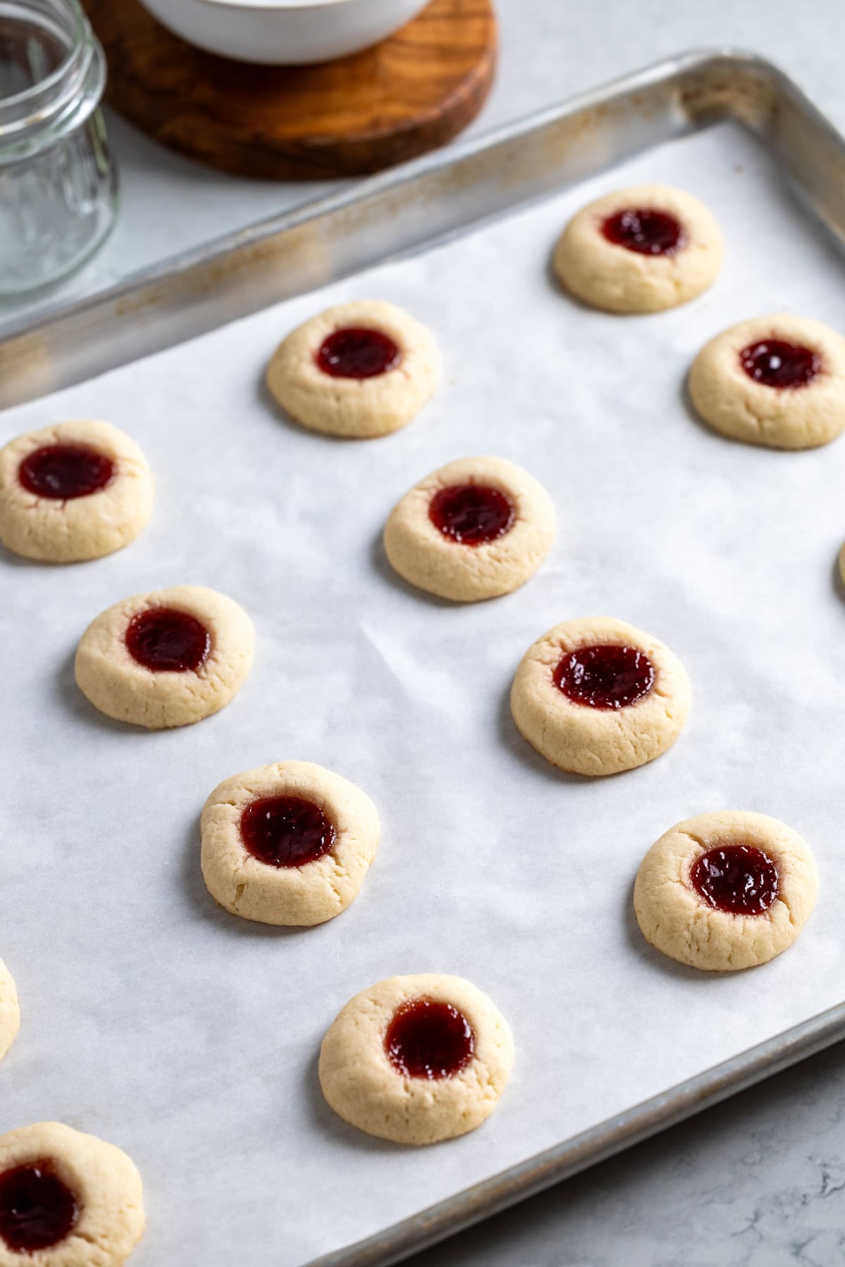 Baked raspberry jam thumbprint cookies on a parchment paper-lined sheet pan.
