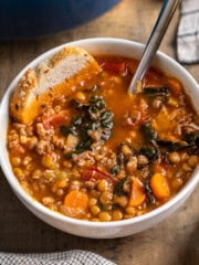 A bowl of Italian lentil soup with sausage with a piece of bread in it.
