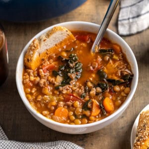 A bowl of Italian lentil soup with sausage with a piece of bread in it.