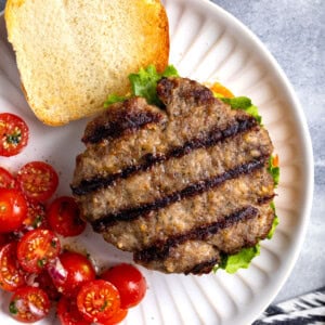 A grilled Italian sausage burger patty on a burger with cherry tomatoes.