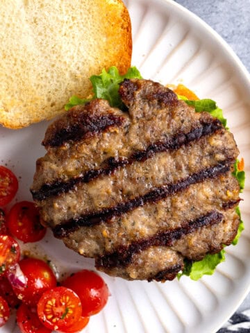 A grilled Italian sausage burger patty on a burger with cherry tomatoes.