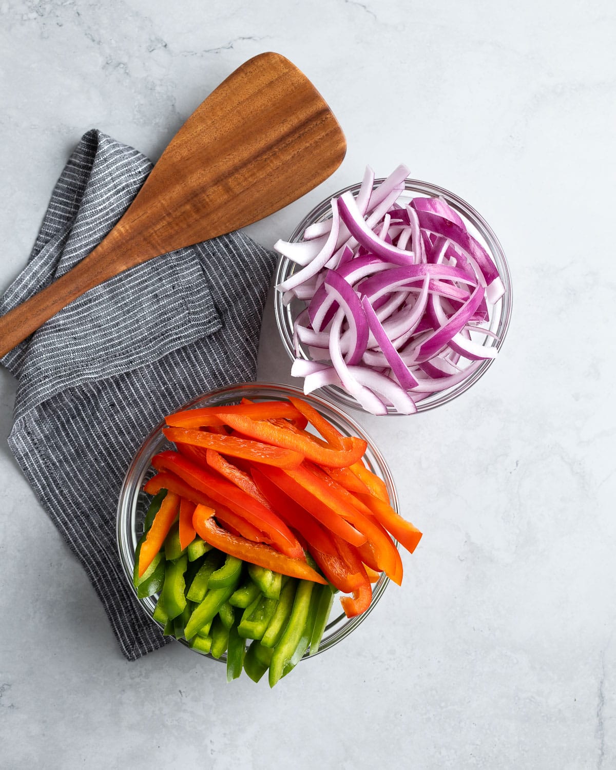 Sliced bell peppers and red onion in bowls.