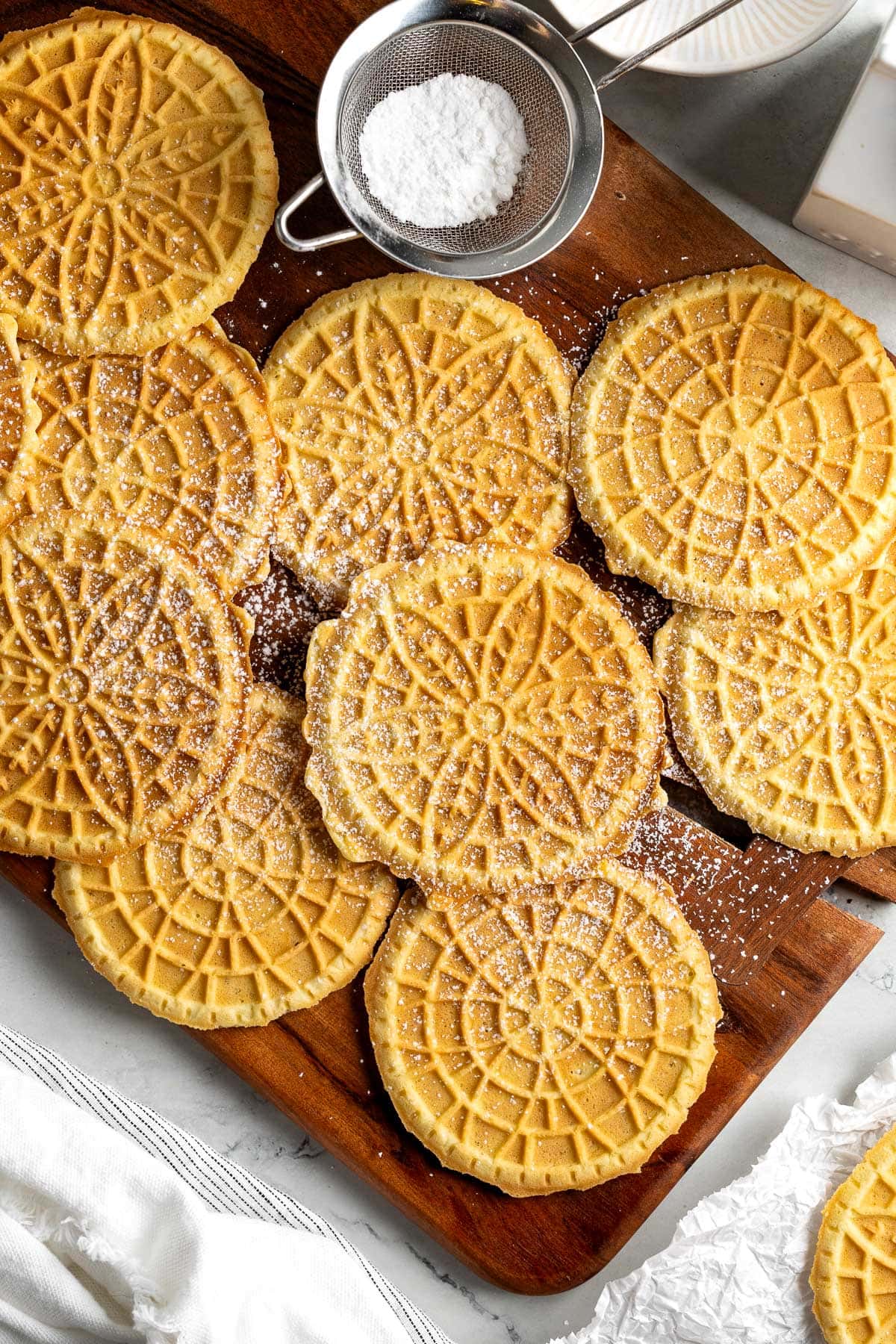 Lemon pizzelle on a wooden board dusted with powdered sugar.