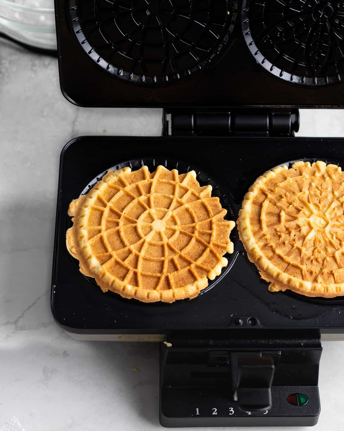 Two lemon pizzelle on the press after being cooked.