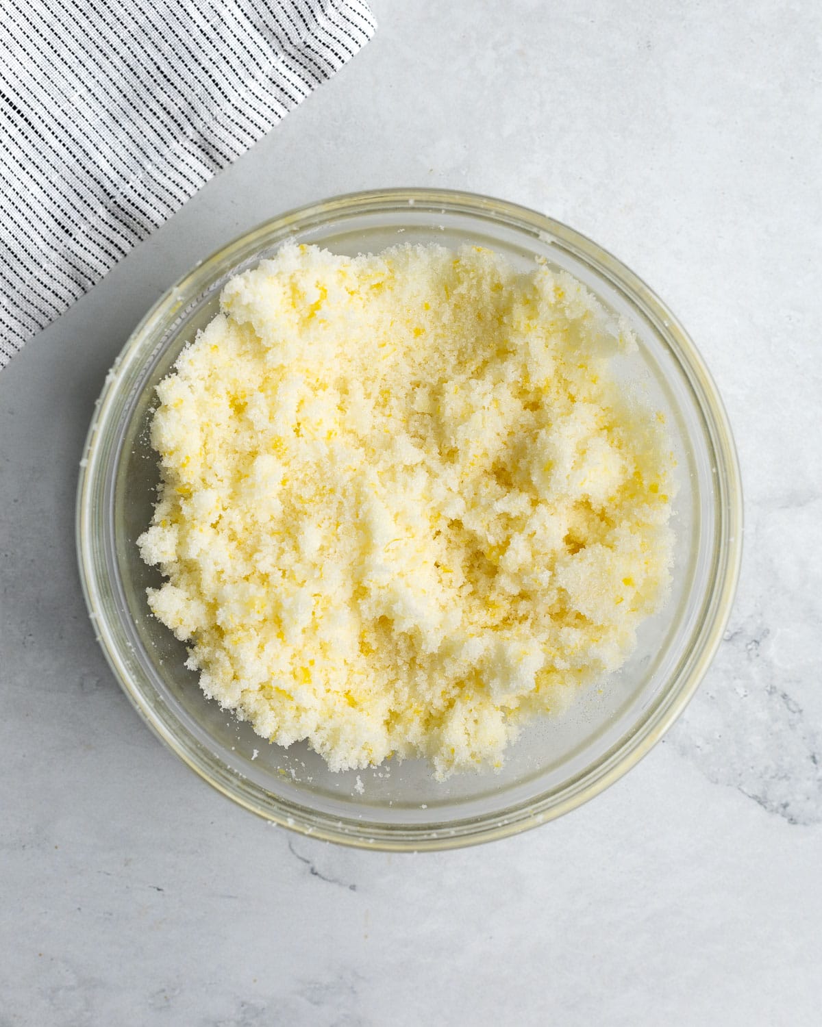 A bowl of lemon zest rubbed into a bowl of granulated sugar.