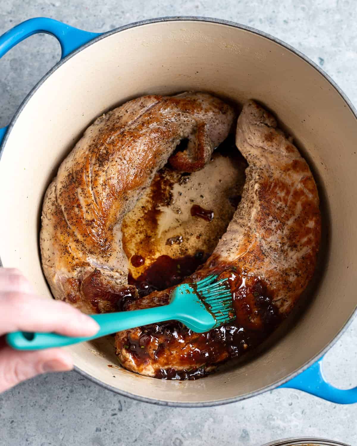 Raspberry balsamic sauce being brushed onto the seared pork tenderloin in a pot.