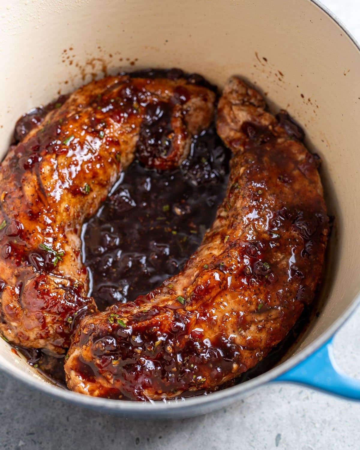Two pork tenderloin pieces cooked in raspberry sauce in a Dutch oven.