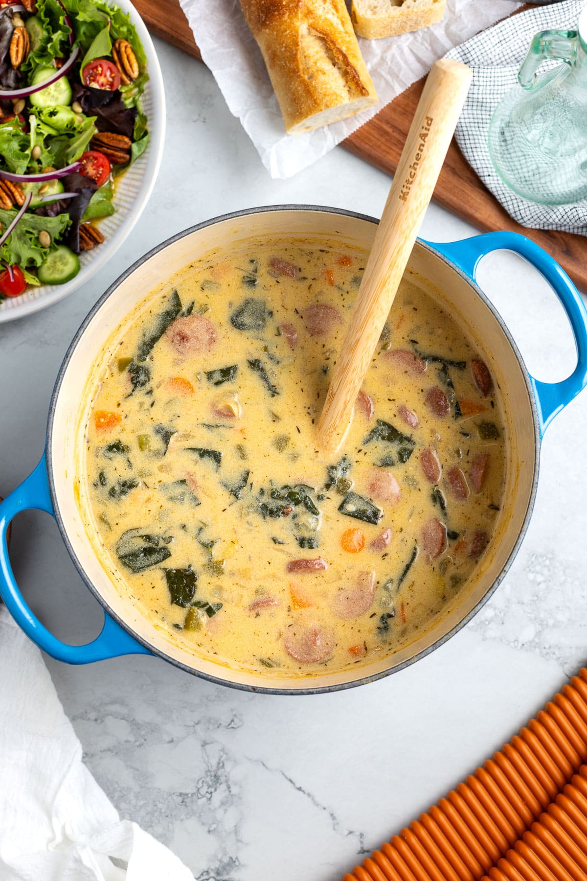 A Dutch oven of smoked sausage and potato soup ready to serve with salad and crusty bread.