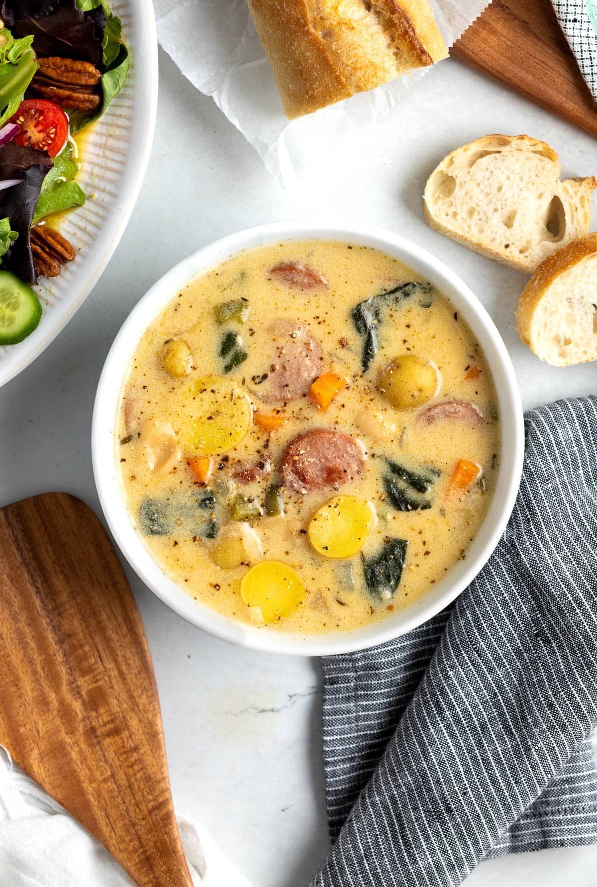 A bowl of soup next to bread and a salad.