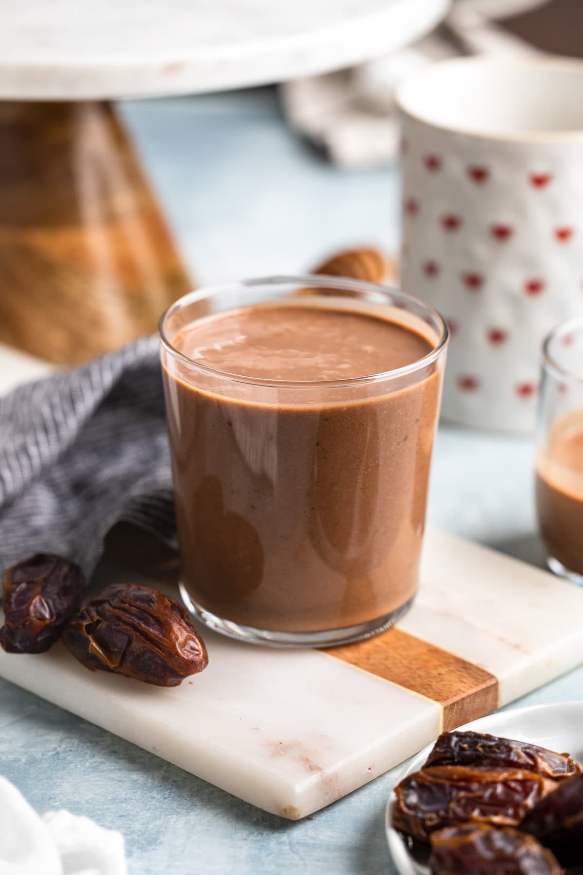 A chocolate date smoothie in a glass surrounded by Medjool dates.