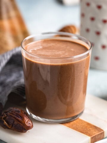 A chocolate date smoothie in a glass surrounded by Medjool dates.